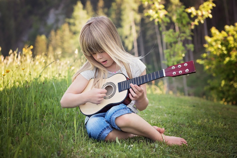 Ein Kind spielt auf einer Wiese Gitarre